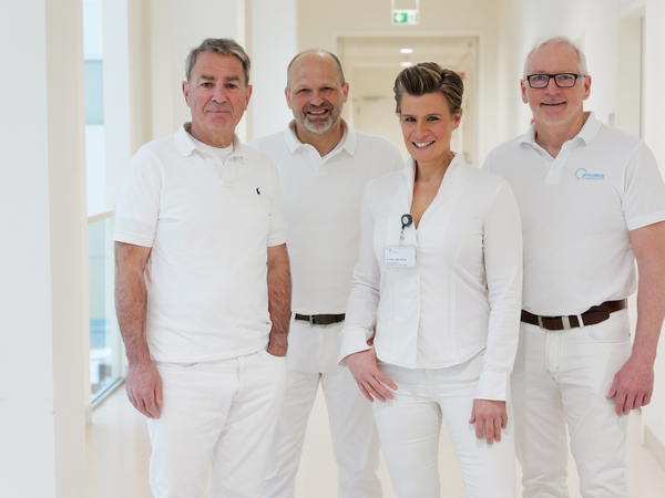 Dr. med. Dirk Rose, Lars Witthöft, Zentrumsleiterin Dr. med. Julia M. Reinke, MHBA, und Dr. med. Bernd Augustin vom Albertinen EndoProthetikZentrum im Albertinen Krankenhaus in Hamburg-Schnelsen stehen in weißer Funktionskleidung in einem Stationsflur und blicken lächelnd in die Kamera.