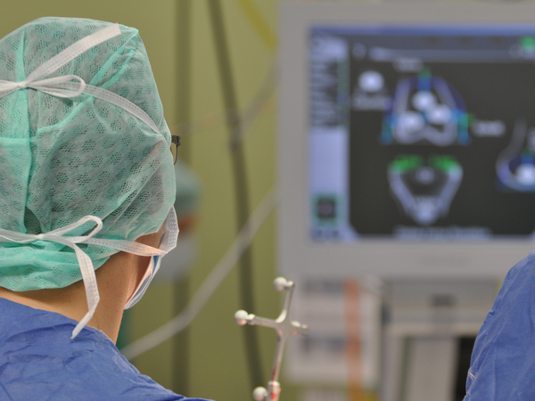 Operateur mit Operationsmaske und Haarnetz blickt auf einen OP-Monitor während einer Operation